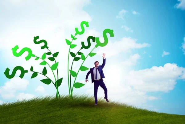 a businessman reaches for the tops of vines with dollar signs at the top.